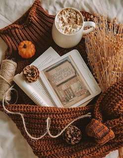 Cozy autumn flat lay with latte, mini pumpkin, book, pinecones, wheat stems, and knitted blanket
