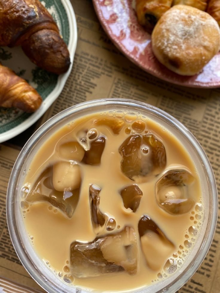 Glass of iced coffee with ice cubes, croissants and pastries on plates viewed from above