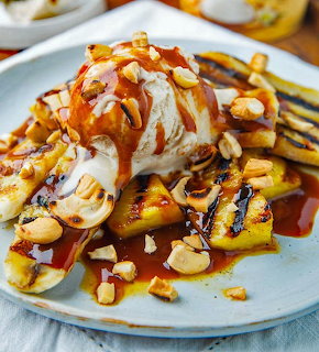 Ice cream sundae with caramel drizzle, grilled fruit, and nuts on a plate
