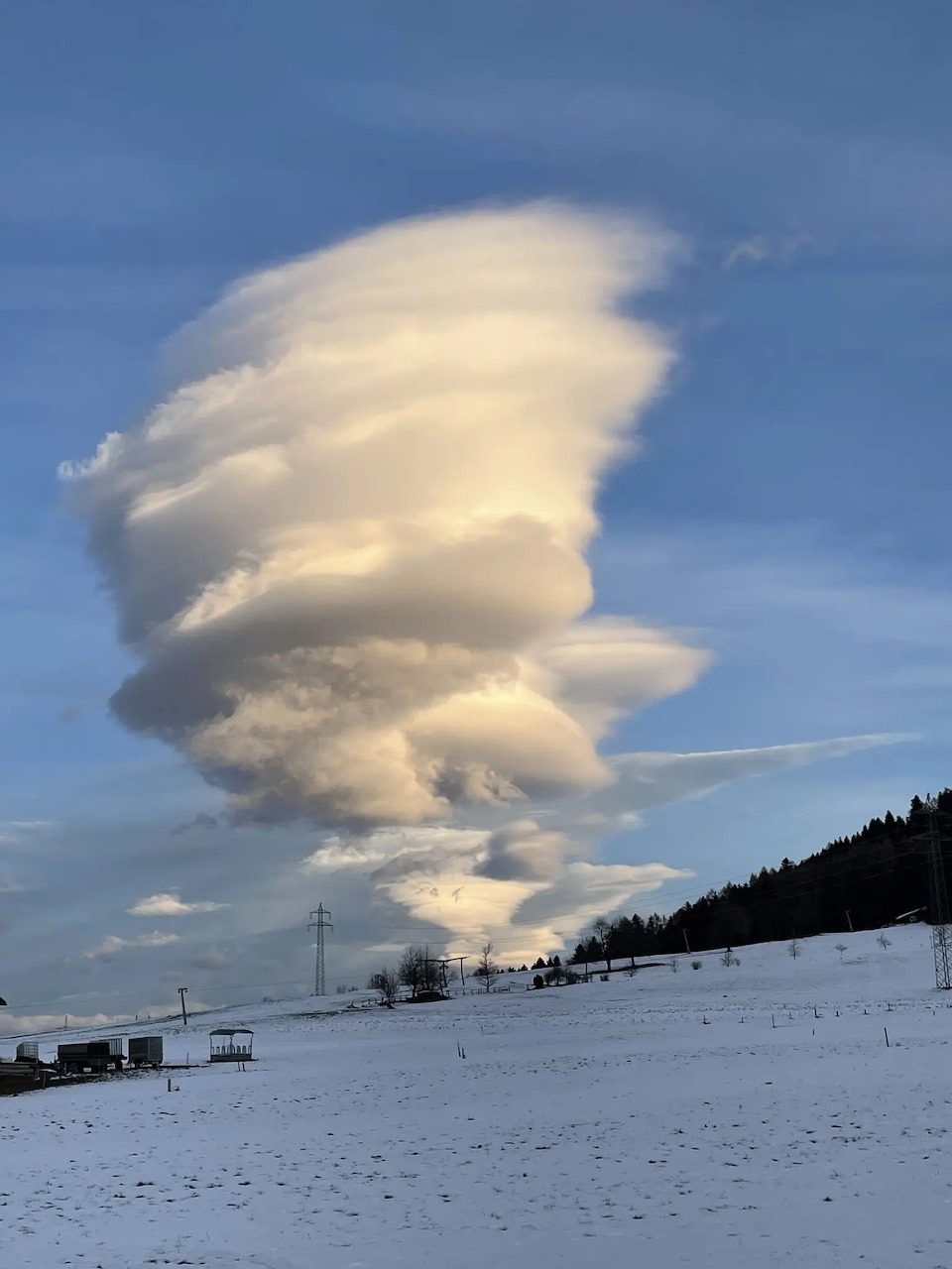 Dramatic stacked lenticular clouds above a snowy field and dark hillside under a blue sky