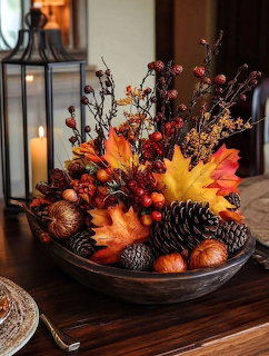 Rustic bowl with autumn decor including pine cones, orange maple leaves, berries, and branches on a wooden table
