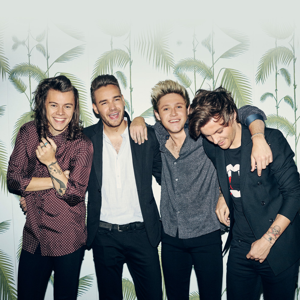 Four young men standing together smiling in front of palm leaf wallpaper
