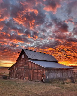 Old wooden barn with metal roof under a colorful dramatic sunset sky with orange and red clouds