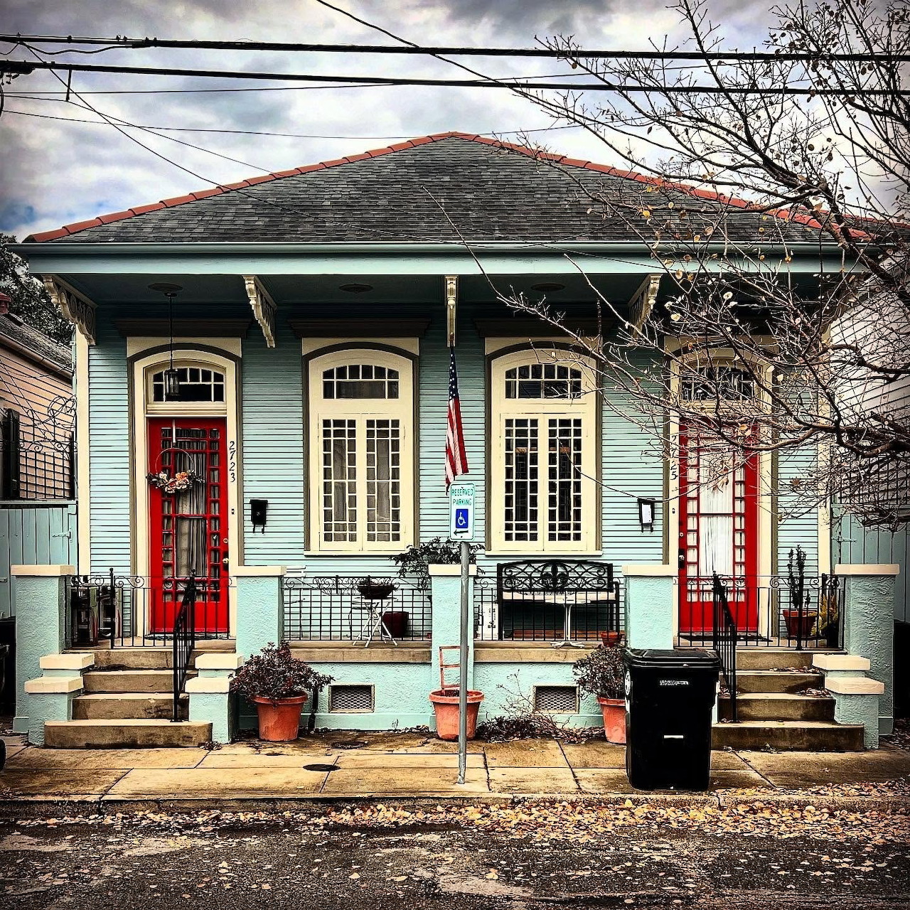 Light blue shotgun house in New Orleans with red doors, shuttered windows, and a front porch