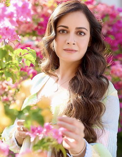 Woman with wavy brown hair surrounded by pink bougainvillea flowers in a garden