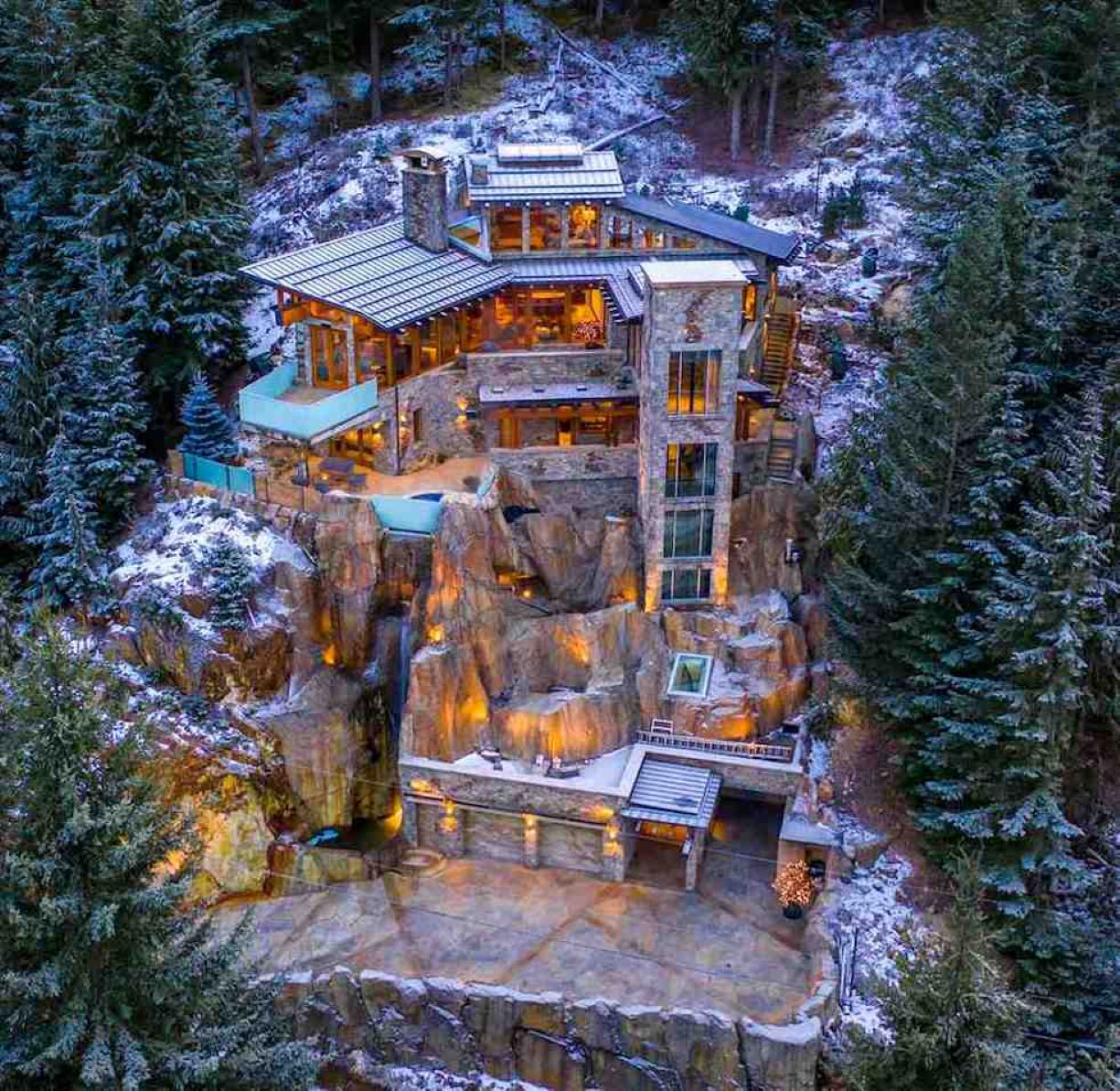 Modern cliffside chalet lit warmly among snowy pine trees at dusk