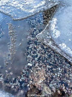 Melting ice and snow revealing pebbles on the rocky shore of Lake Superior