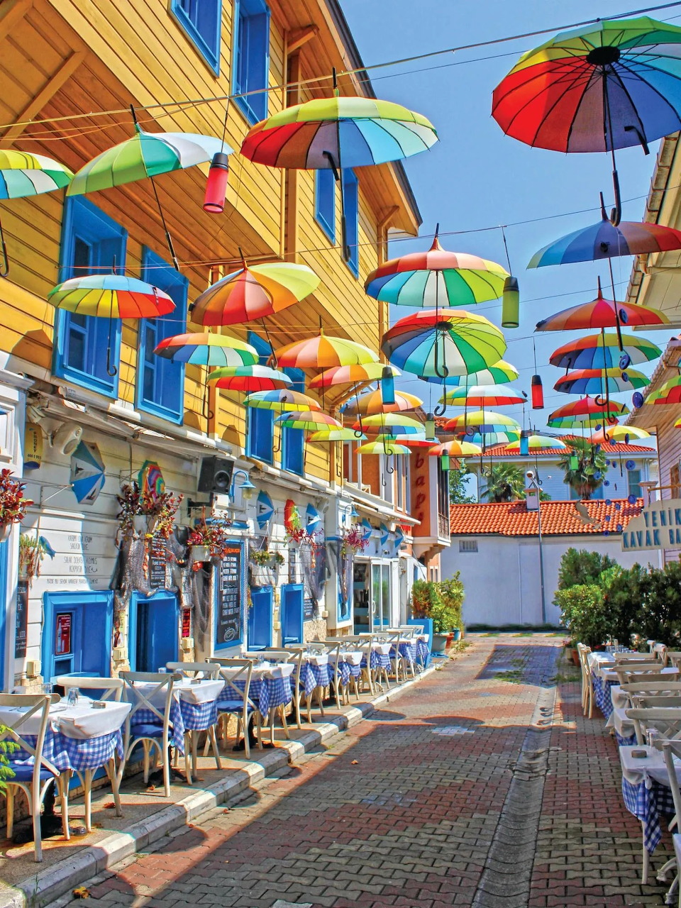 Colorful floating parasols hanging above an outdoor cafe street with white and blue tables and chairs
