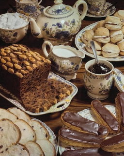Teapot and cups with cake, cookies, bread, and chocolate pastries on a wooden table