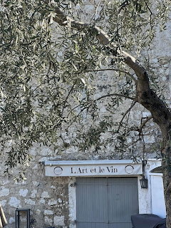Olive tree against old stone wall above a shop entrance sign reading L'Art et le Vin in Saint-Paul-de-Vence