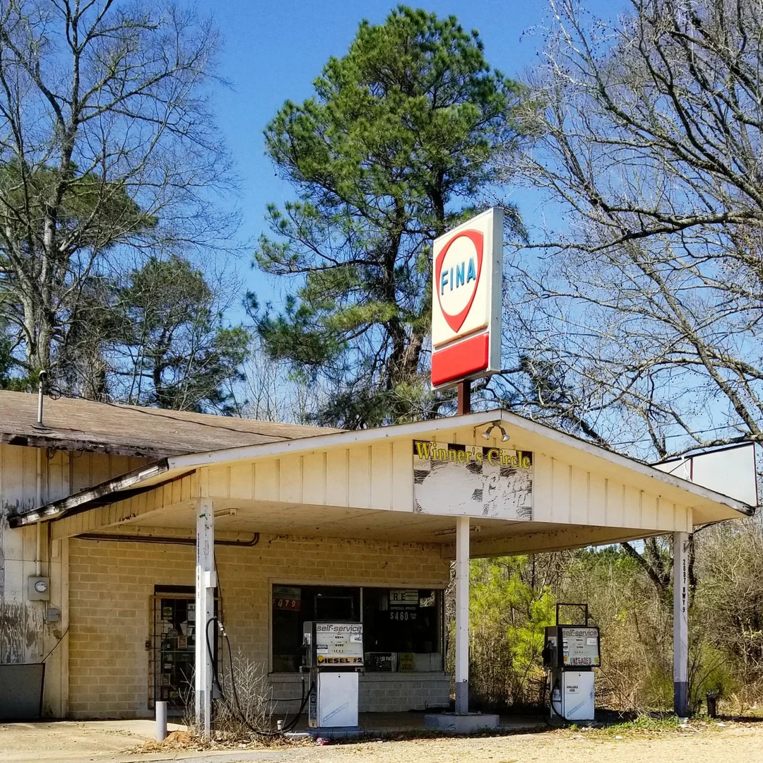 Old brick service station with vintage gas pumps and a Fina sign by the roadside