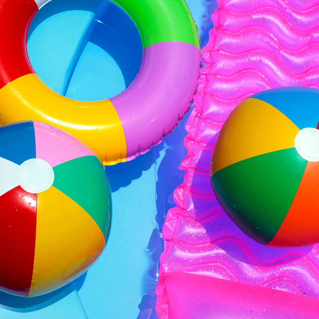 Colorful striped beach balls floating in blue pool water with pink inflatable rafts
