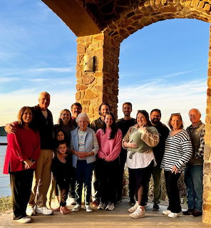 Large family group posing under a stone arch with ocean and blue sky in the background
