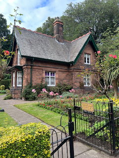 Red brick Victorian cottage with decorative chimneys, lush garden, and iron gate entrance