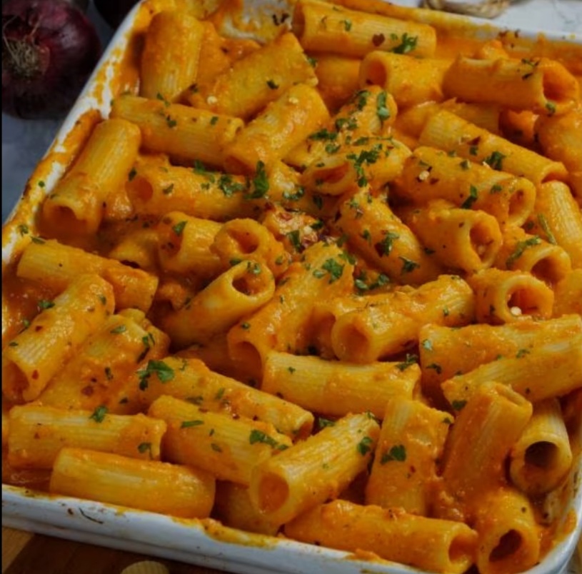 Rigatoni pasta in orange sauce with herbs in a white baking dish