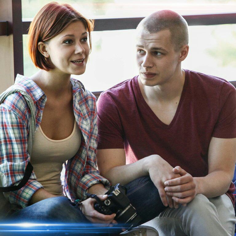 Young woman and man sitting indoors by a window, with the woman holding a camera