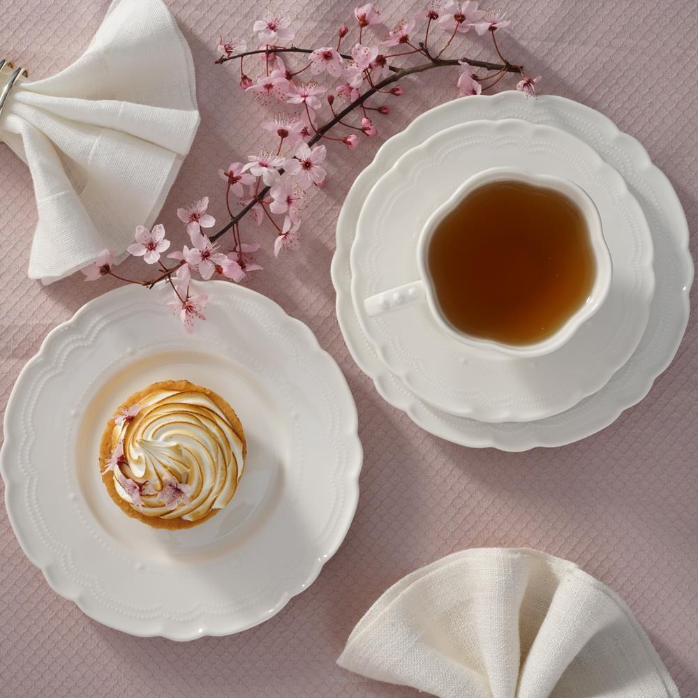 Flatlay of tea in white cup, swirled pastry on plate, napkins, and cherry blossoms on pink cloth