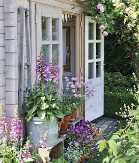 Cottage porch decorated with colorful potted flowers and climbing plants beside white French doors