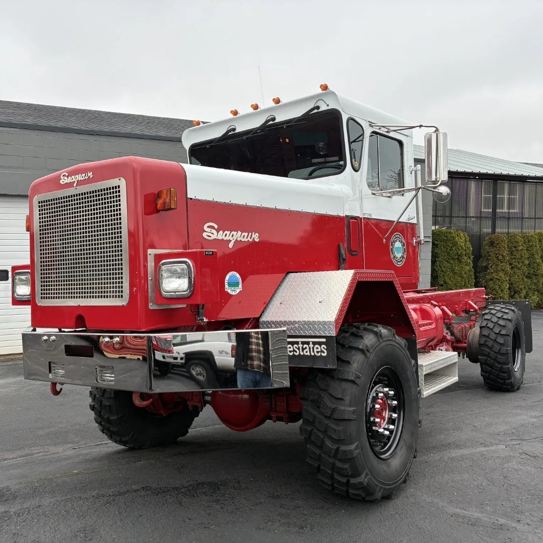 Red and white Seagrave heavy-duty truck parked outside industrial buildings