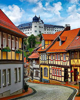 Colorful half-timbered houses on cobblestone street with castle on hill above in German village