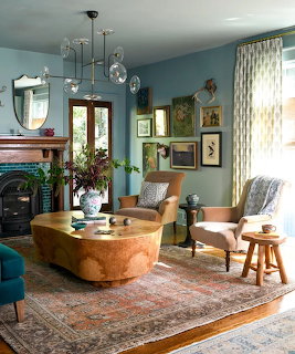 Eclectic living room with blue walls, glass chandelier, vintage rug, armchairs, and gallery wall