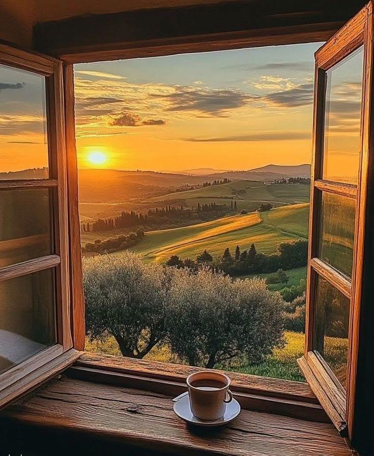 Open window with sunset over rolling hills and a coffee cup on the sill