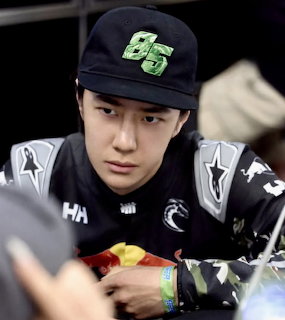 Young Asian man in black cap with number 85 and dark graphic jacket looking downward