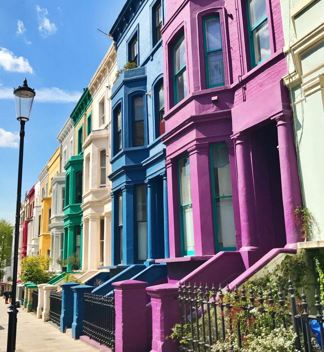 Colorful row houses with ornate bay windows and front steps in bright pink, blue, yellow, and green along a sunny street