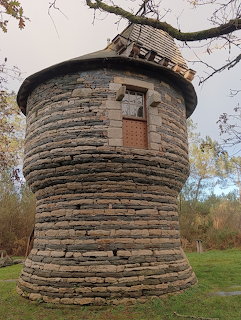 Round stone dovecote tower with layered masonry and slate roof under autumn trees