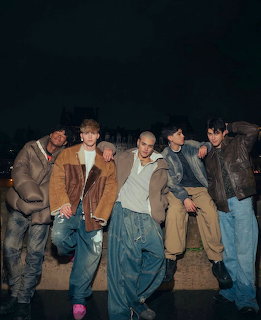 Four young men posing outdoors at night in casual jackets and baggy jeans