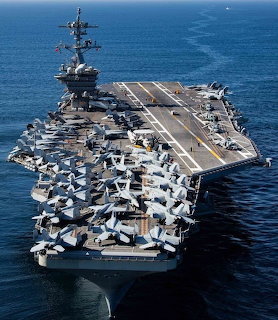 Aerial view of USS Abraham Lincoln aircraft carrier with fighter jets on flight deck sailing on blue ocean