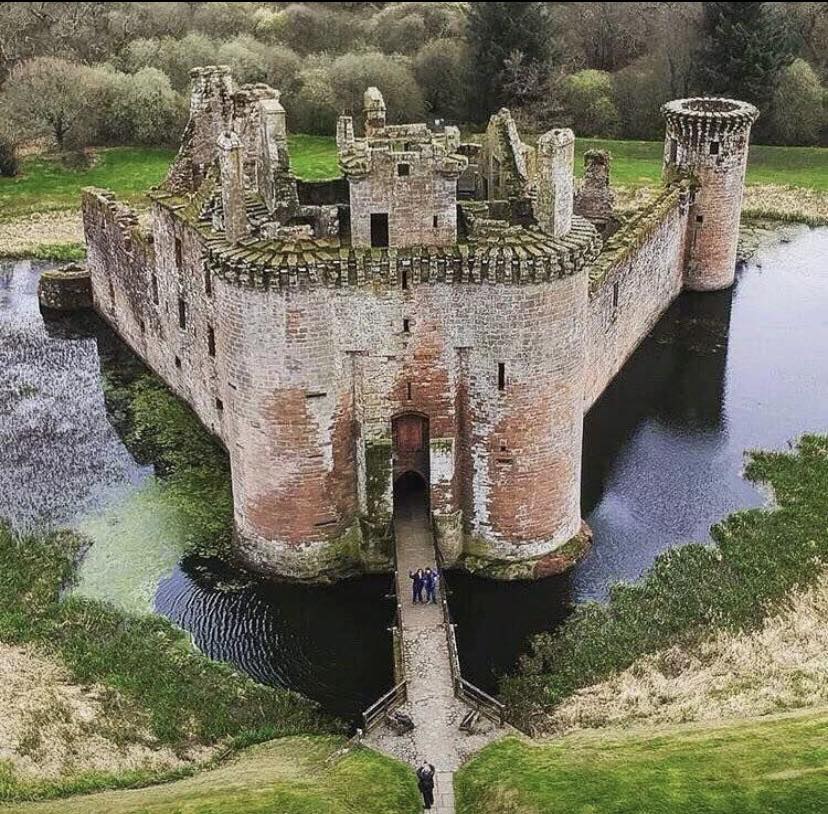 Aerial view of triangular Caerlaverock Castle surrounded by moat with weathered stone walls and round towers