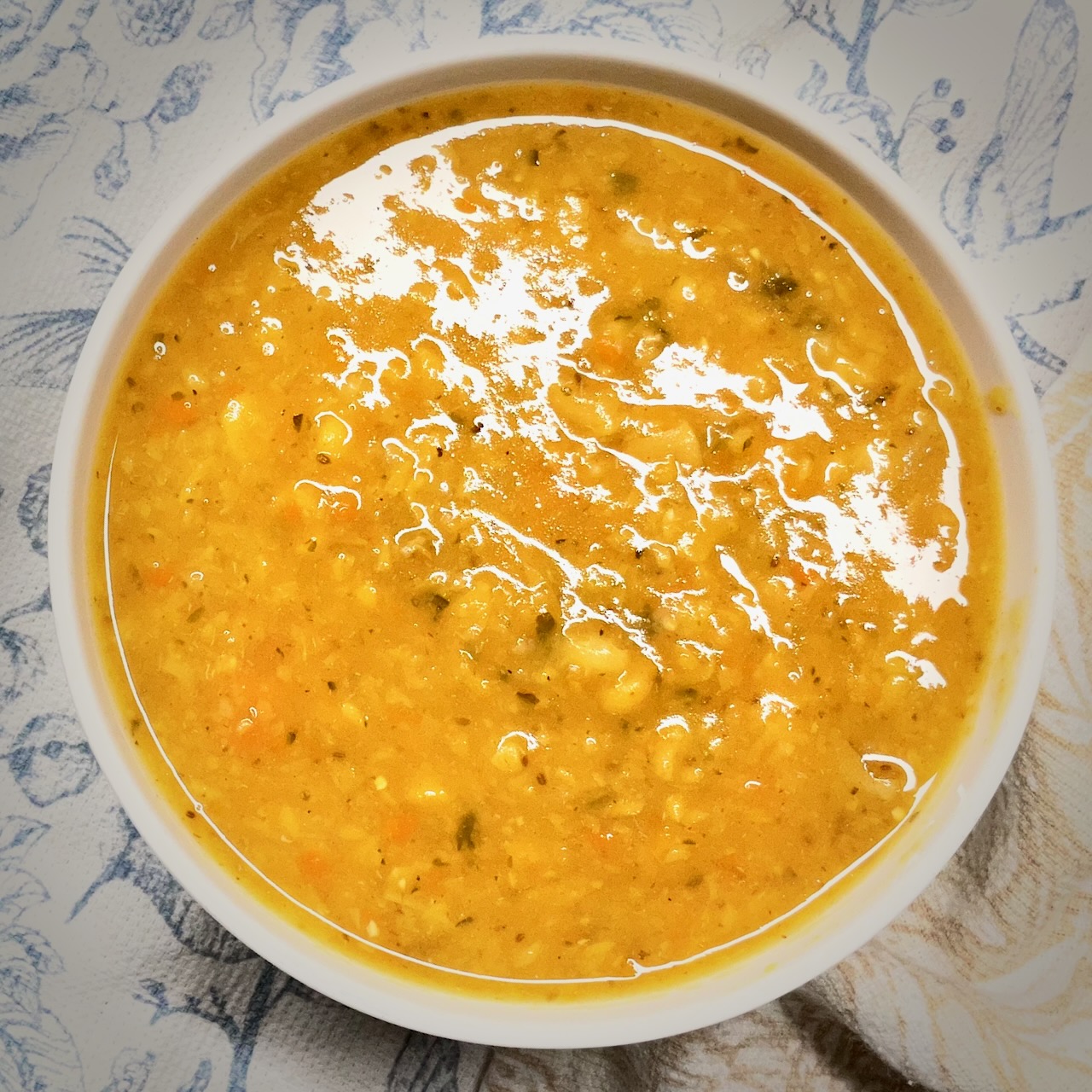 Top view of a bowl of yellow split pea soup on a light patterned tablecloth