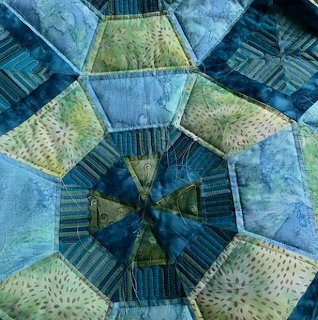 Hexagonal patchwork quilt in blue and green tones with decorative stitching