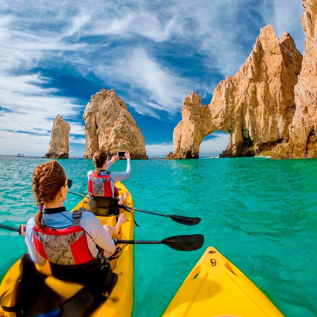 Two kayakers in yellow kayaks on turquoise water near the rocky arches of Los Cabos