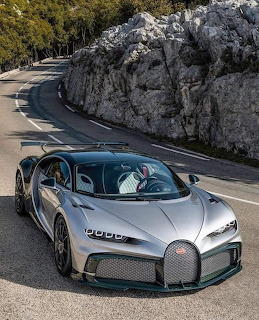 Silver sports car on a curving mountain road beside a rocky rock face