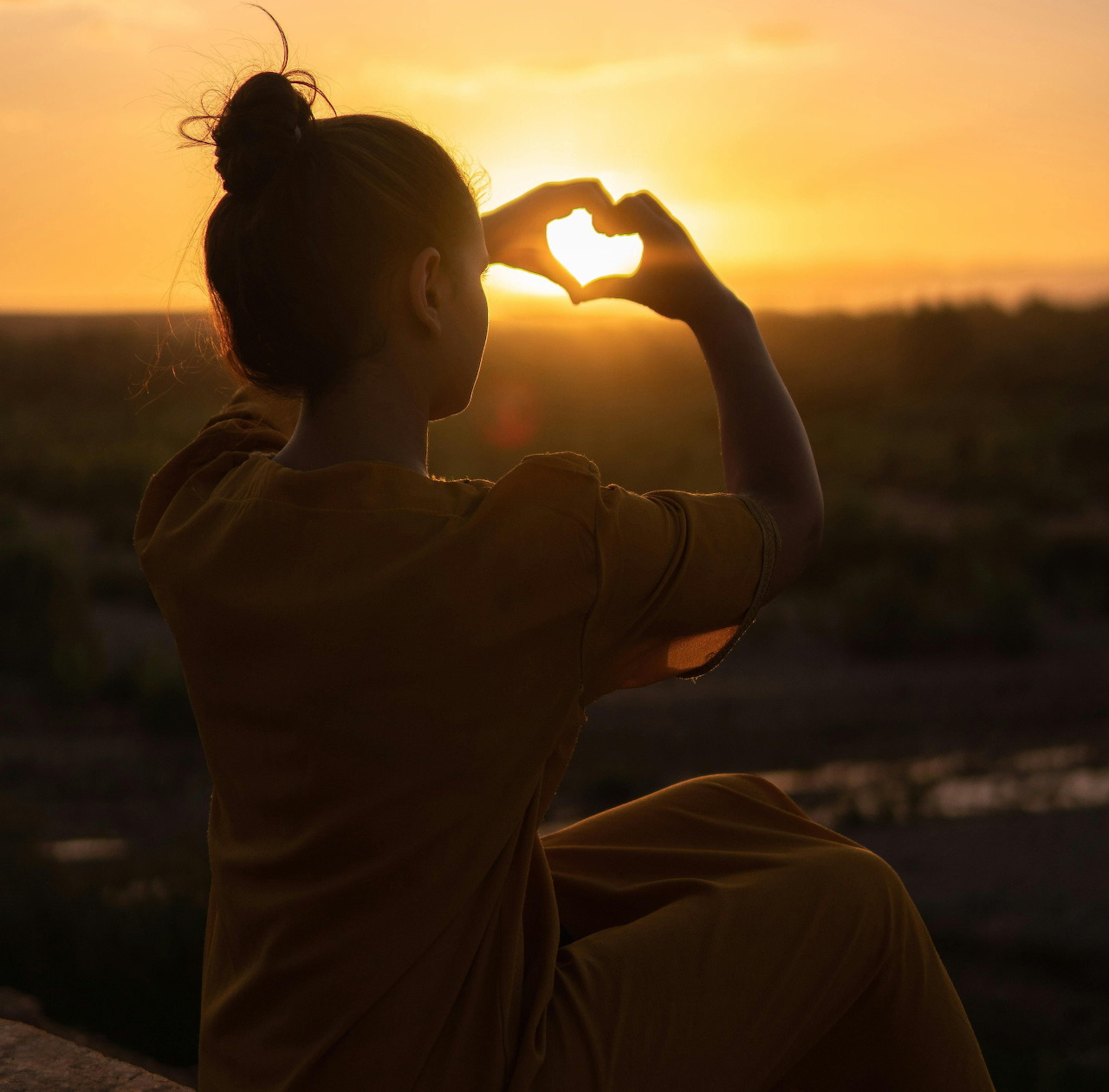 Silhouette of a woman making a heart shape with her hands at sunset