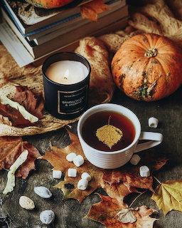 Autumn flatlay with tea cup, lit candle, pumpkins, fall leaves, and marshmallows on rustic background