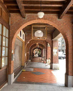 Covered brick arcade with arched columns, tiled floor, and wooden storefronts