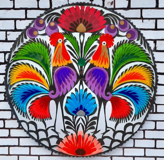 Two colorful folk-art roosters in a circular floral pattern on a white brick background