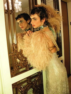 Woman in gold sequined dress and feathered wrap posing elegantly with mirror reflection