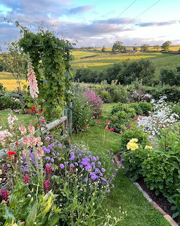 Colorful English country garden with mixed flower borders and green countryside beyond