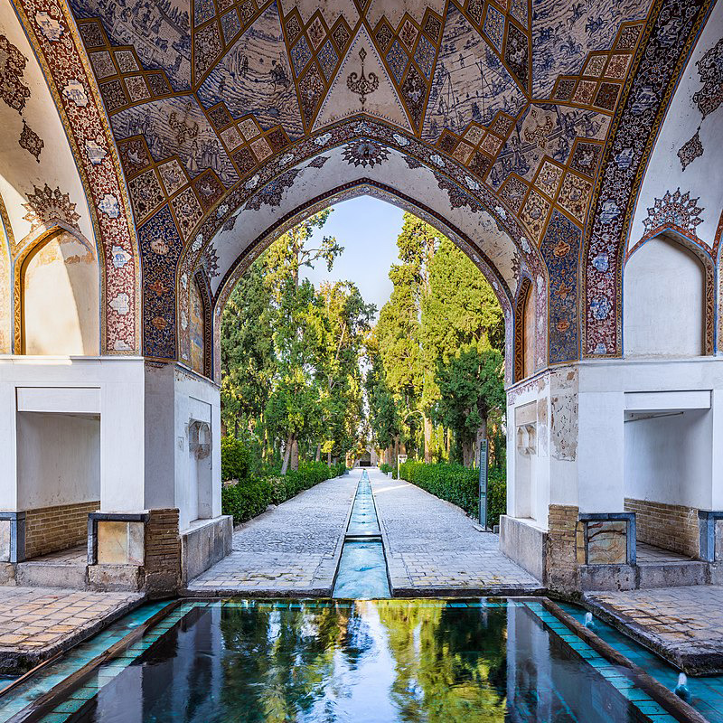 Tiled archway overlooking a Persian garden path and reflecting pool lined with trees