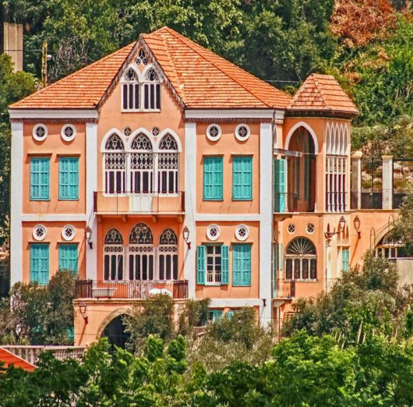 Traditional Lebanese house with arched windows and orange tile roof amid greenery