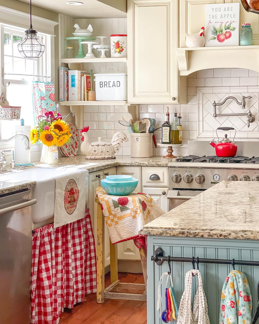 Bright vintage farmhouse kitchen with white cabinets, floral textiles, sunflowers, and a red kettle