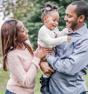 Smiling parents holding their happy toddler daughter outdoors in a park setting