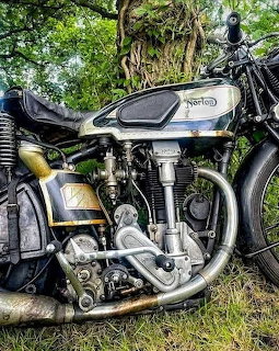 Vintage Norton International motorcycle engine and frame closeup on grass with trees behind