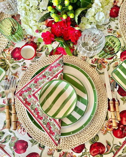 Overhead view of elegant table setting with green striped plates, floral napkins, wicker chargers and red flowers