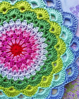 Colorful crocheted mandala with pink center, white, yellow, green, and blue layered rings in decorative stitch patterns