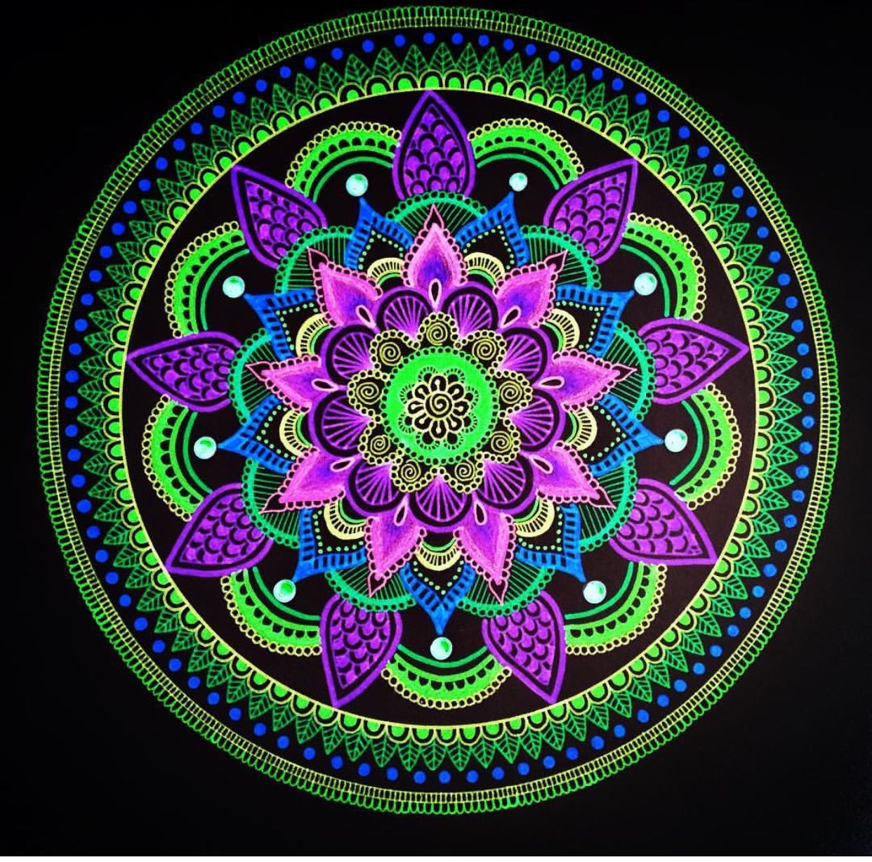 Circular mandala with purple flowers, green borders, and blue accents on black background